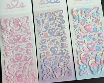 May include: Three vertical sticker sheets labeled Pink Gradation Confetti with a heart logo. Each sheet features various holographic shapes including swirls, hearts, and small dots in pink, purple, and blue gradients on a clear backing.