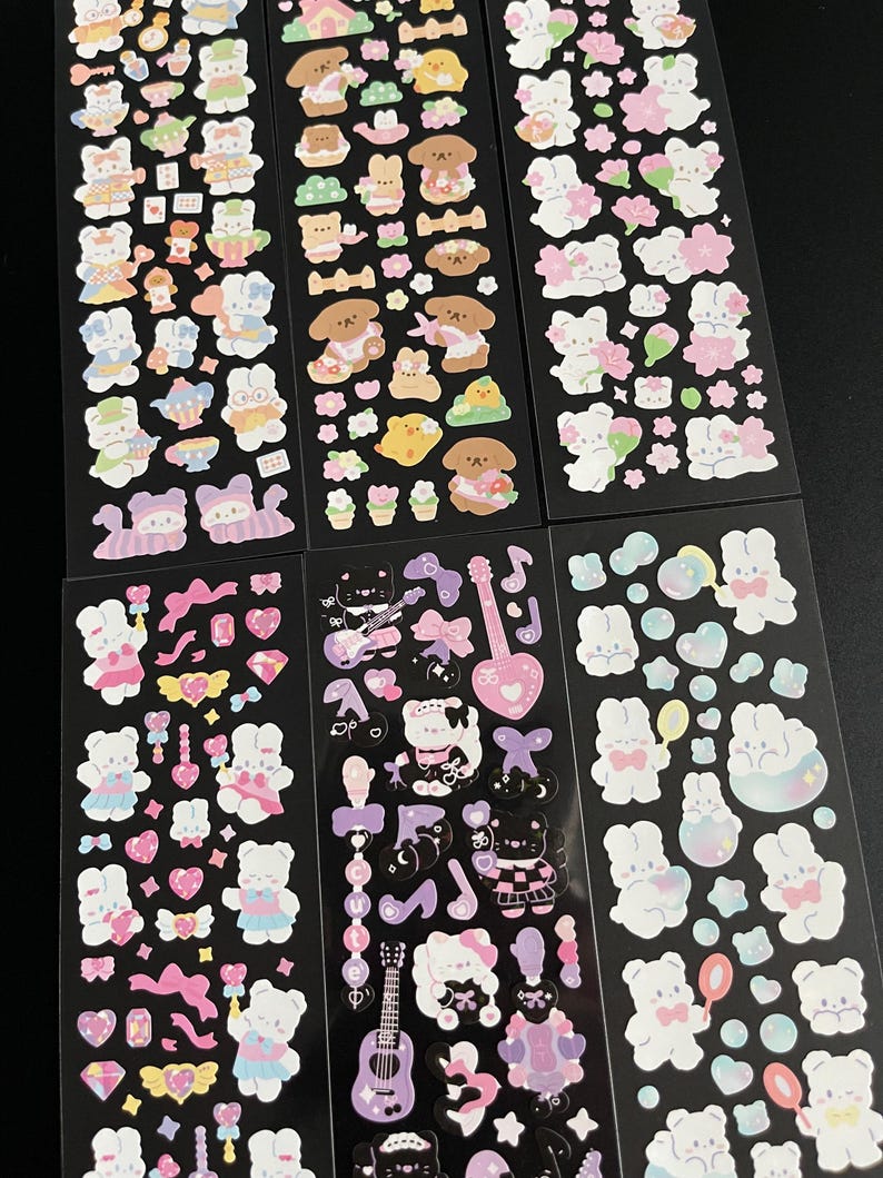 May include: A sheet of stickers featuring cute cartoon bunnies in various poses and outfits. The stickers are on a black background and include a variety of designs, including hearts, stars, flowers, and musical notes.