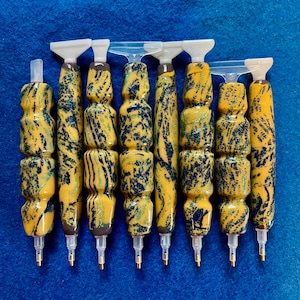 Pode incluir: Conjunto de sete canetas para pintura de diamantes com alças marmoreadas amarelas e azuis e pontas de plástico transparentes.