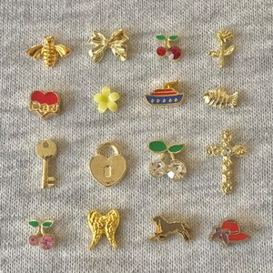 May include: A selection of small, gold-coloured charms and embellishments. The charms include a bee, bow, cherries, rose, heart with "Dad" text, flower, boat, fish, key, heart-shaped lock, cherries, cross, cherries, angel wings, horse, and a hat.