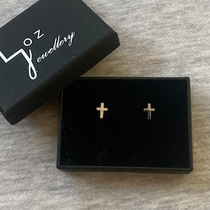 May include: A pair of gold cross stud earrings in a black jewelry box with the text "Joz Jewellery" on the lid.
