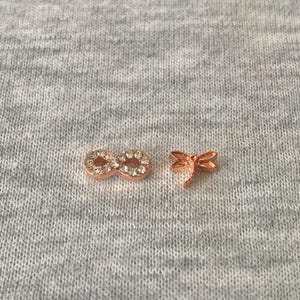 May include: Two rose gold charms on a grey surface. One is an infinity symbol with clear crystals. The other is a dragonfly. The charms are small and delicate.