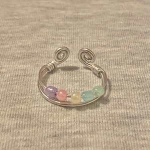 May include: A silver wire ring with pastel coloured beads. The beads are purple, pink, yellow, blue, and green.