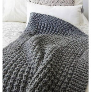 May include: A gray knitted blanket with a textured pattern is draped over a bed. The blanket transitions from a darker gray at the top to a lighter gray at the bottom. The text "ORLINGBURY Knitted blanket pattern" is visible.