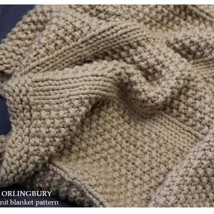 May include: Close-up of a beige knitted blanket with a textured, woven pattern. The blanket has a thick, chunky knit design with visible stitches. The text "ORLINGBURY Knit blanket pattern" is visible in the lower left corner.