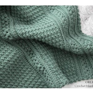 May include: Close-up of a sage green crochet blanket. The blanket has a textured stitch pattern with vertical ribbed sections. The text "ORLINGBURY Crochet blanket pattern" is visible in the bottom right corner.