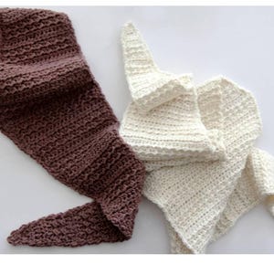 May include: Two handmade crochet scarves. One is a deep brown color, and the other is off-white. The scarves are made with a textured stitch, and are folded and draped on a white surface. The brown scarf is long and narrow, while the off-white scarf is folded.