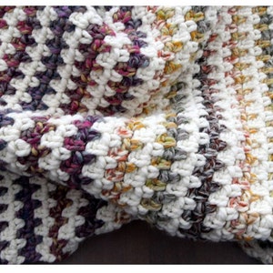 May include: A close-up of a crocheted blanket with a white background and stripes of various colors, including purple, pink, yellow, and brown.