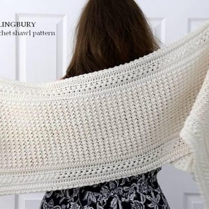 May include: Cream-colored crochet shawl held by a person. The shawl features a detailed openwork design with textured borders. Text in the image reads "ORLINGBURY Crochet shawl pattern".