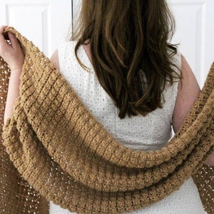 Può includere: Un scialle di uncinetto marrone drappeggiato sulle spalle di una persona. Lo scialle ha un motivo a pizzo ed è realizzato con un filato morbido.