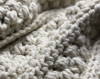 May include: Close-up of a cream-colored crocheted blanket with a textured, woven pattern.