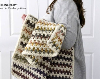 May include: A crocheted blanket in a multi-colored striped pattern with shades of brown, cream, and beige. The blanket is folded and held by a person.