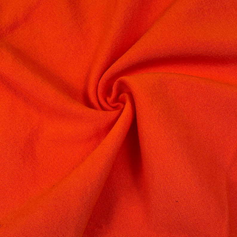 May include: Close-up of a vibrant orange fabric with a textured surface. The material is gathered and swirled, creating a dynamic pattern of folds and shadows. The bright color suggests a textile suitable for clothing or home decor.