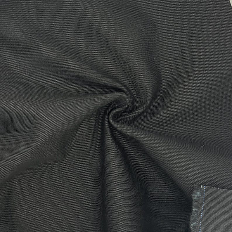 Puede incluir: Una tela negra s&oacute;lida con un patr&oacute;n de tejido de sarga diagonal distintivo. El material est&aacute; recogido en el centro, creando pliegues suaves y sombras que resaltan la textura densa y duradera de la superficie textil y su color oscuro.