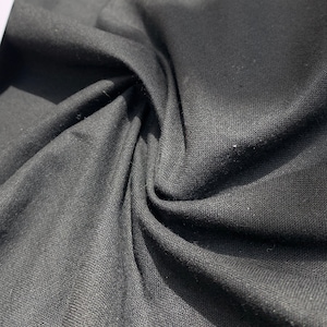 May include: Black fabric with a textured weave. The fabric is folded and draped, showing its soft, drapey texture.