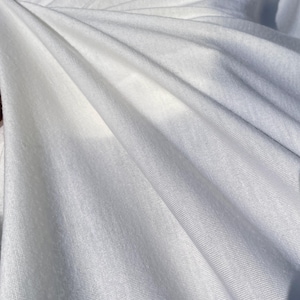 May include: White fabric with a smooth, slightly textured surface. The fabric is draped and folded, creating soft, flowing lines.