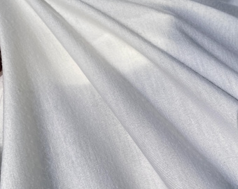 May include: White fabric with a smooth, slightly textured surface. The fabric is draped and folded, creating soft, flowing lines.