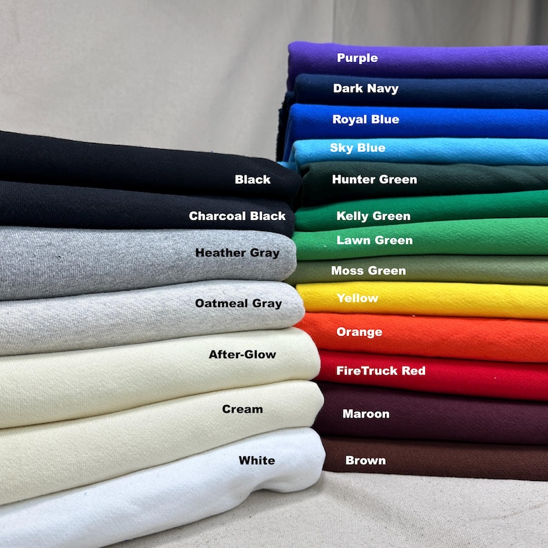 May include: A stack of fabric swatches in various colors, including black, charcoal black, heather gray, and white. Other colors include purple, dark navy, royal blue, sky blue, hunter green, and more. Each swatch is labeled with its color name.