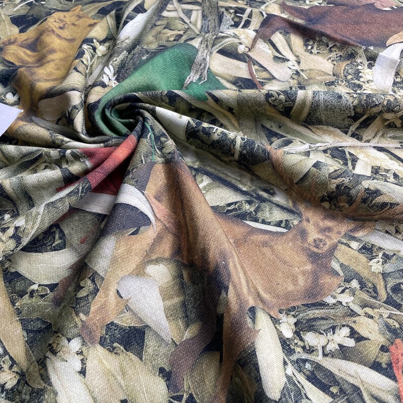 May include: Camouflage fabric with a brown, green, and white pattern. The fabric features a repeating design of leaves, branches, and deer silhouettes.