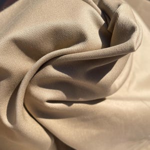May include: A close-up of a beige fabric with a subtle ribbed texture. The fabric is folded and draped, showcasing its soft and smooth surface.