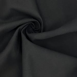 Puede incluir: Una tela negra s&oacute;lida con una textura tejida apretada y distintiva. El material est&aacute; recogido en el centro, creando pliegues profundos y suaves y sombras que resaltan el acabado mate uniforme y el tejido consistente del material textil.