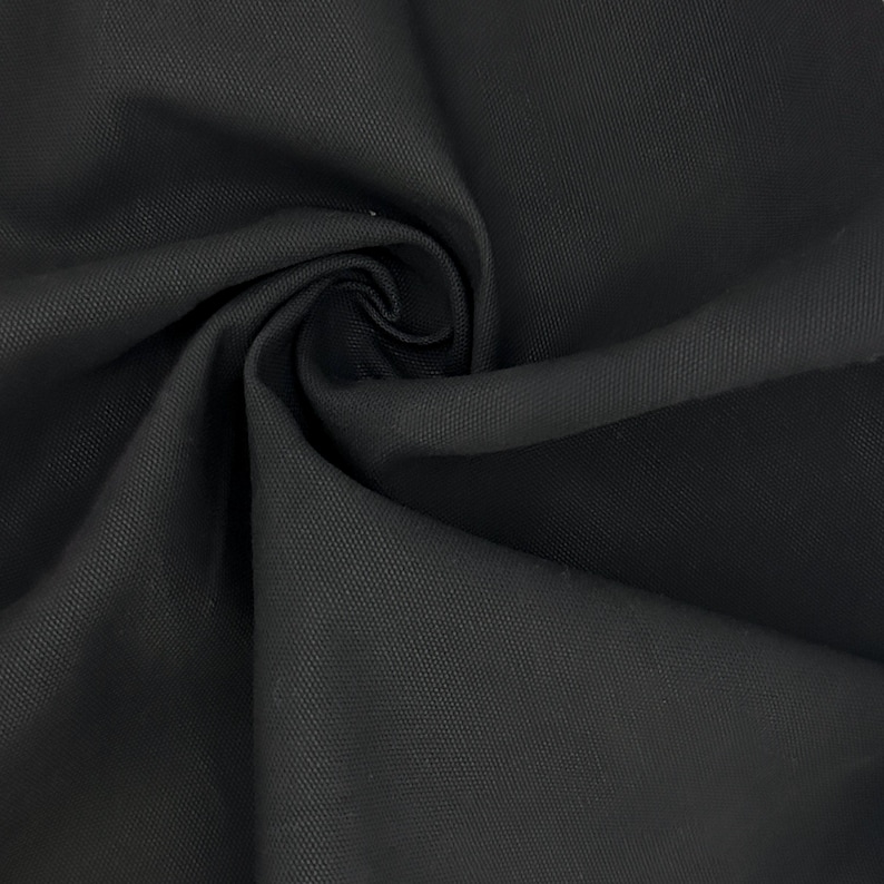 Puede incluir: Una tela negra s&oacute;lida con una textura tejida apretada y distintiva. El material est&aacute; recogido en el centro, creando pliegues profundos y suaves y sombras que resaltan el acabado mate uniforme y el tejido consistente del material textil.