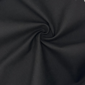 Puede incluir: Una tela negra s&oacute;lida con una textura de tejido fino y uniforme. El material est&aacute; recogido en el centro, creando pliegues suaves y radiantes junto con sombras que resaltan el acabado mate y el color oscuro constante de la superficie.