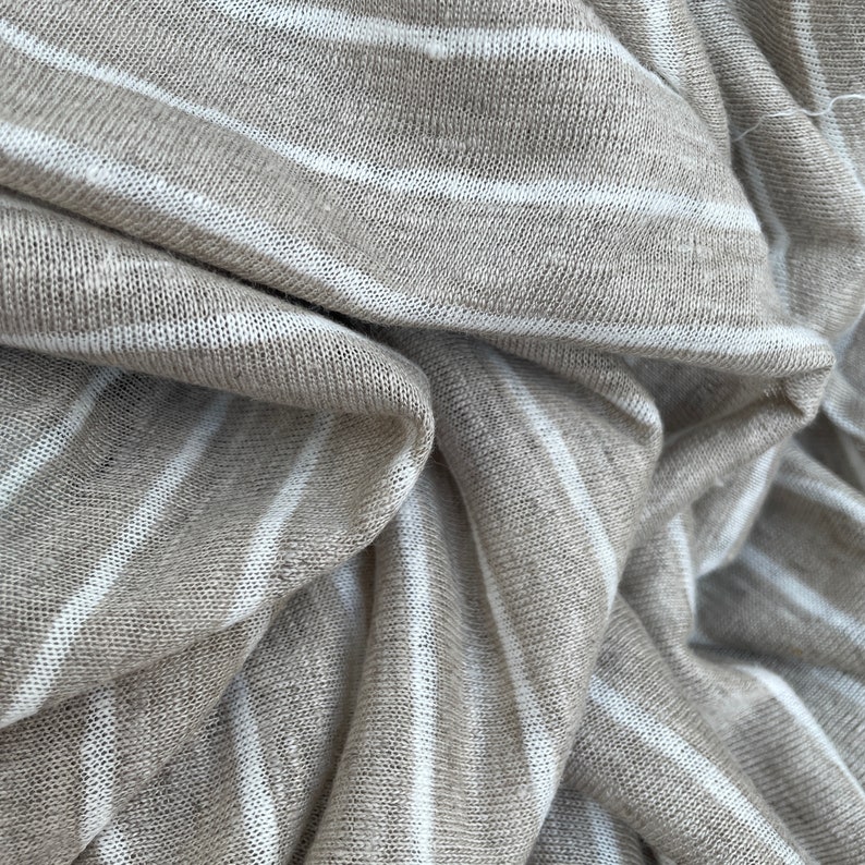 May include: Close-up of a beige and white striped fabric. The fabric is soft and has a slightly textured surface.