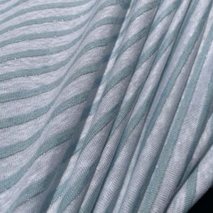 May include: White fabric with thin, light blue stripes. The fabric has a subtle shimmer.