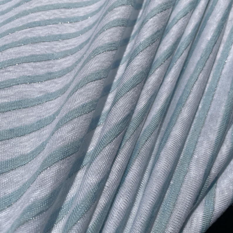 May include: White fabric with thin, light blue stripes. The fabric has a subtle shimmer.