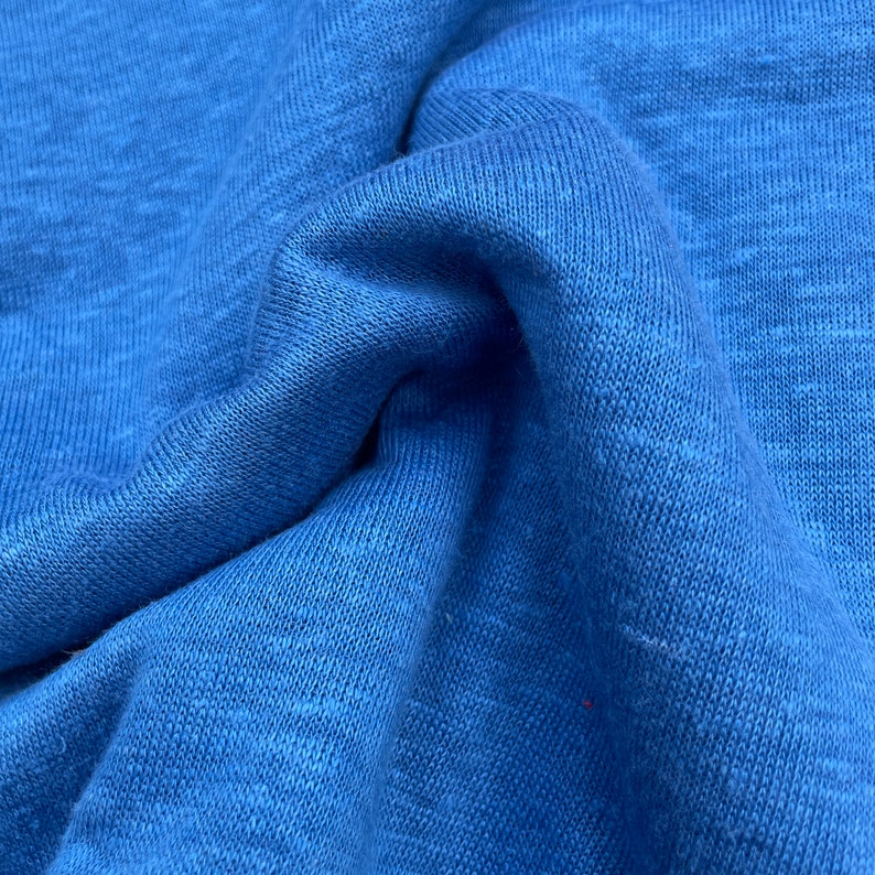 May include: Close-up of a blue fabric with a textured, slightly rough surface. The fabric is folded and wrinkled, showing its texture.