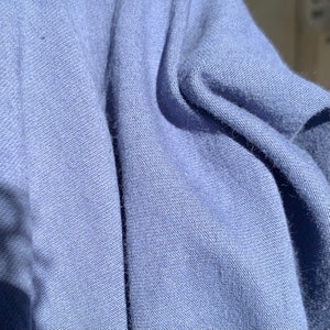 May include: Close-up of a soft, blue fabric with a textured weave. The fabric is folded and draped, showing the subtle texture and light catching on the surface.