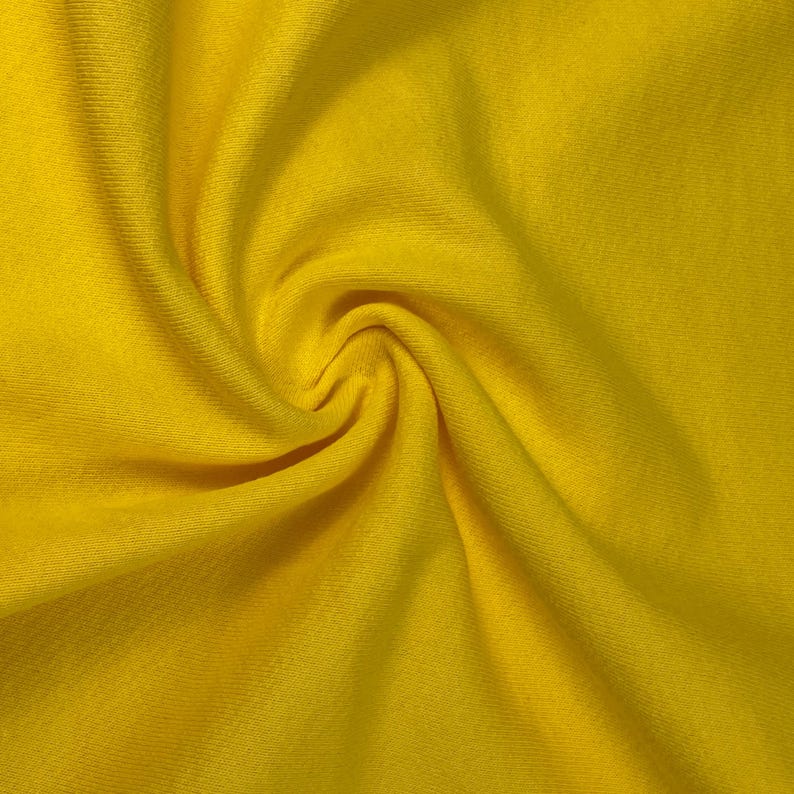 May include: Close-up of a vibrant yellow fabric with a soft, textured appearance. The material is gathered and swirled, creating a dynamic pattern of light and shadow. The bright color suggests a textile suitable for clothing or home decor.