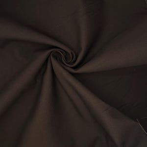 Puede incluir: Una tela de color marr&oacute;n oscuro con una textura tejida visible, que presenta un remolino central o pliegue fruncido que crea sombras y reflejos suaves y radiantes en la superficie del material, destacando su acabado mate y color profundo.
