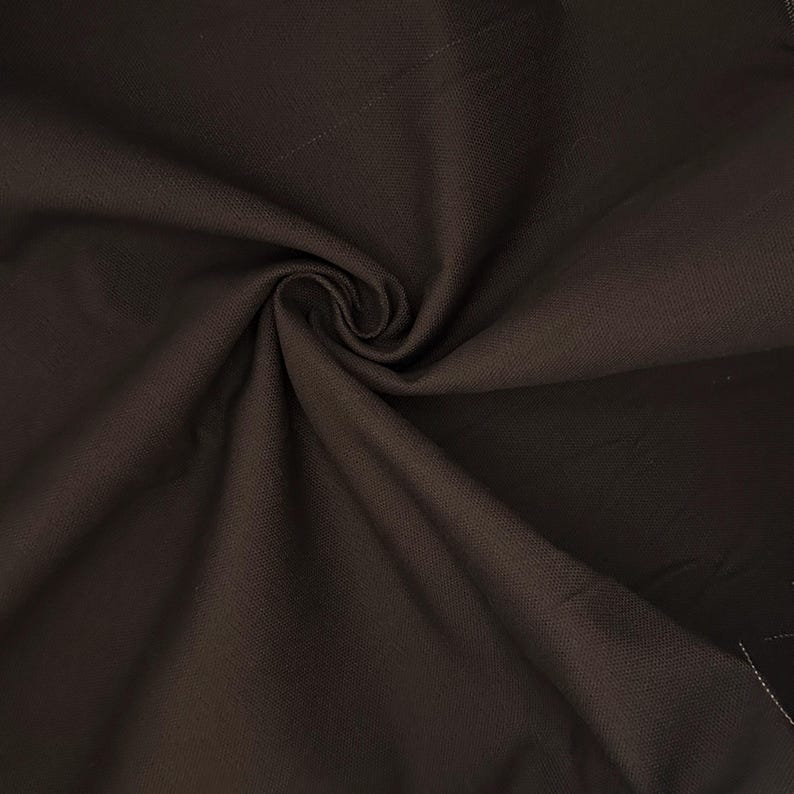 Puede incluir: Una tela de color marr&oacute;n oscuro con una textura tejida visible, que presenta un remolino central o pliegue fruncido que crea sombras y reflejos suaves y radiantes en la superficie del material, destacando su acabado mate y color profundo.