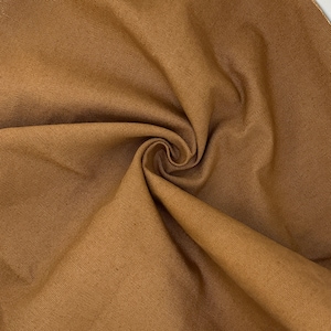 Puede incluir: Una tela de color marr&oacute;n s&oacute;lido con una textura tejida visible. El material est&aacute; recogido en el centro, creando pliegues suaves y sombras que resaltan el tono terroso consistente y el tejido apretado y uniforme de la superficie textil.