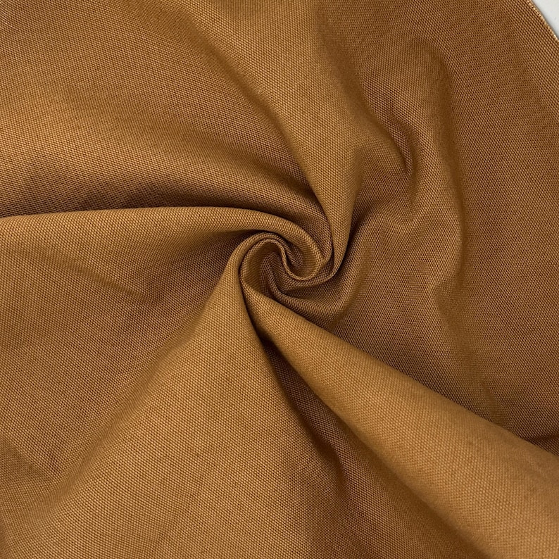 Puede incluir: Una tela de color marr&oacute;n s&oacute;lido con una textura tejida visible. El material est&aacute; recogido en el centro, creando pliegues suaves y sombras que resaltan el tono terroso consistente y el tejido apretado y uniforme de la superficie textil.