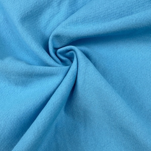 May include: Close-up of a folded piece of light blue fabric. The fabric has a soft texture and is tightly woven. The color is a bright, solid blue, with subtle variations in tone due to the folds. The image highlights the texture and color of the material.