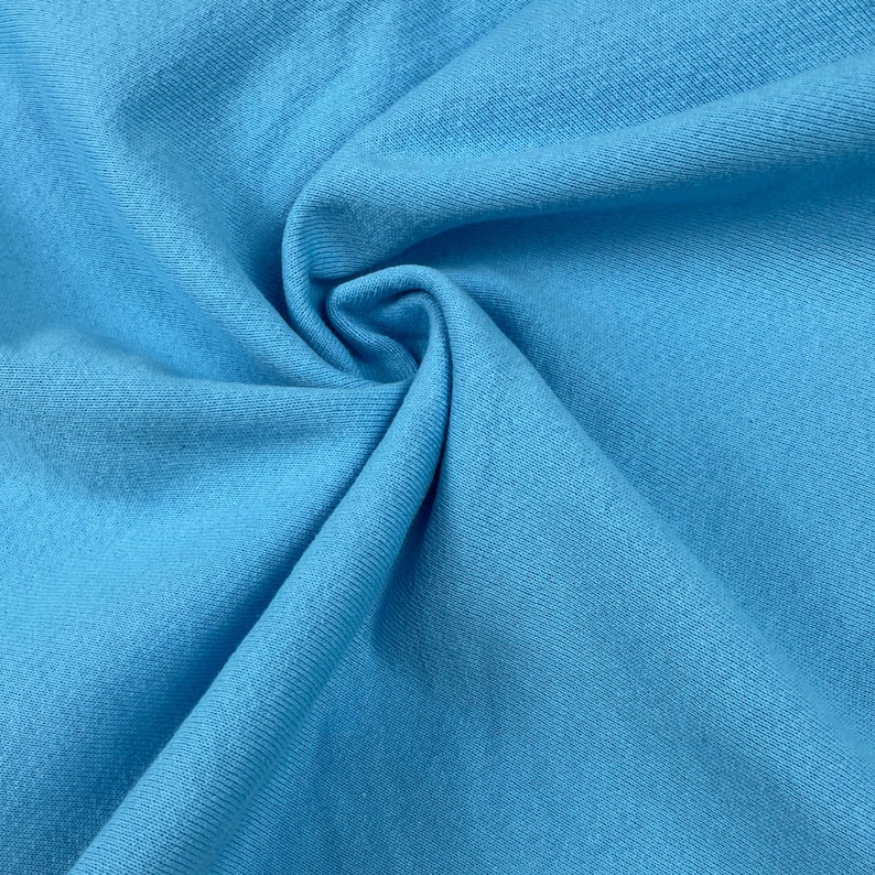 May include: Close-up of a folded piece of light blue fabric. The fabric has a soft texture and is tightly woven. The color is a bright, solid blue, with subtle variations in tone due to the folds. The image highlights the texture and color of the material.