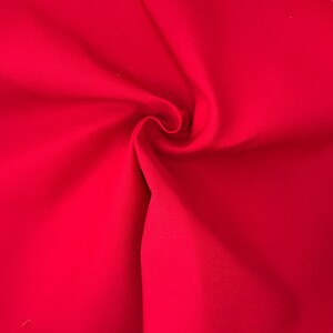 Puede incluir: Una tela de color rojo vibrante con una textura tejida visible, que presenta pliegues y drapeados suaves que crean sombras y reflejos naturales en la superficie. El material muestra un color s&oacute;lido y consistente con un tejido denso y apretado.