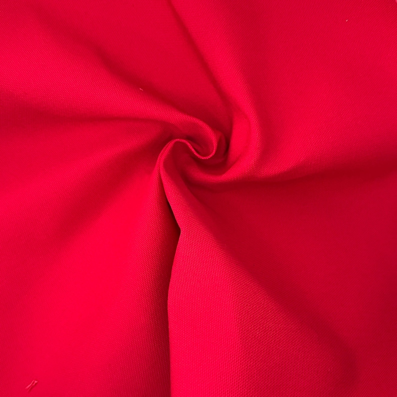 Puede incluir: Una tela de color rojo vibrante con una textura tejida visible, que presenta pliegues y drapeados suaves que crean sombras y reflejos naturales en la superficie. El material muestra un color s&oacute;lido y consistente con un tejido denso y apretado.