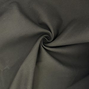Puede incluir: Una tela de color gris carb&oacute;n oscuro con una textura tejida visible. El material est&aacute; recogido en el centro, creando pliegues profundos y fluidos y sombras que resaltan el tejido denso y uniforme de la superficie textil en toda la imagen.