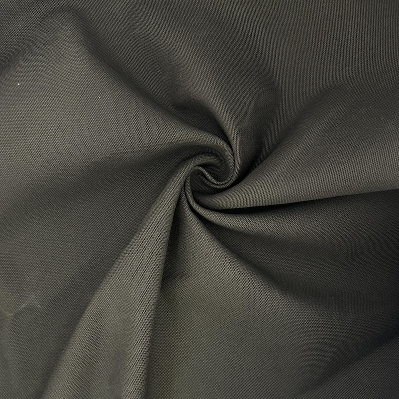 Puede incluir: Una tela de color gris carb&oacute;n oscuro con una textura tejida visible. El material est&aacute; recogido en el centro, creando pliegues profundos y fluidos y sombras que resaltan el tejido denso y uniforme de la superficie textil en toda la imagen.