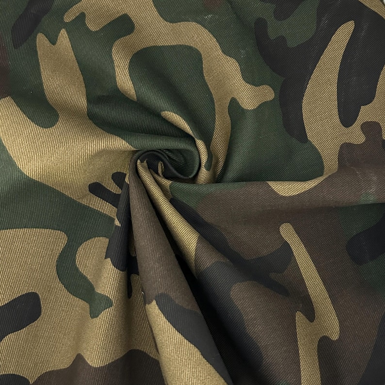 Puede incluir: Una tela con un patr&oacute;n de camuflaje cl&aacute;sico en tonos verde oliva, marr&oacute;n oscuro, bronceado y negro. El material tiene una textura visible de tejido de sarga diagonal y est&aacute; recogido en el centro para crear pliegues y sombras suaves.