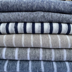 May include: Stack of six striped fabric swatches in various shades of blue, gray, and white. The fabric is a linen blend and has a textured appearance.