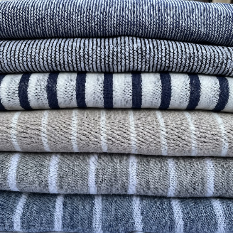 May include: Stack of six striped fabric swatches in various shades of blue, gray, and white. The fabric is a linen blend and has a textured appearance.
