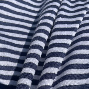 May include: White and navy blue striped fabric with a subtle shimmer. The fabric is folded and draped, showing the texture and pattern.