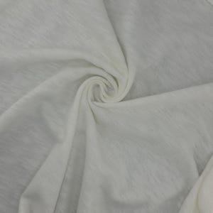 Puede incluir: Primer plano de una tela blanca con un aspecto suave y texturizado. La tela est&aacute; tejida apretadamente, con un ligero brillo, y est&aacute; dispuesta en un patr&oacute;n arremolinado. El material parece ligero y transpirable, adecuado para ropa.