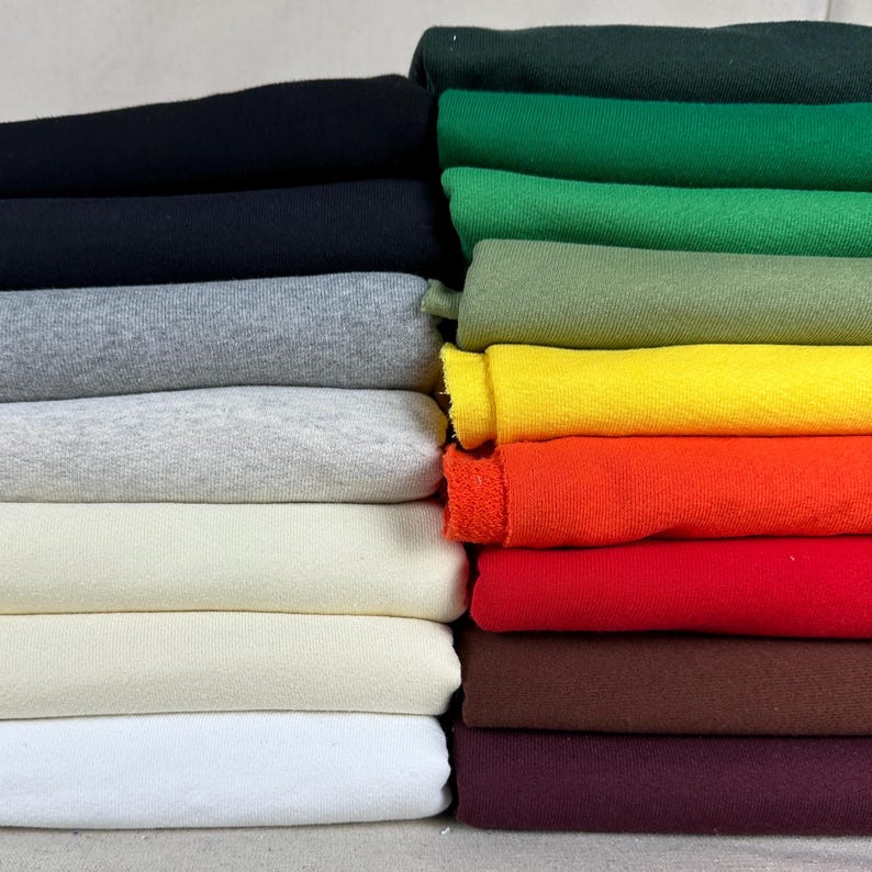 May include: A stack of folded fabric in various colors, including black, gray, white, yellow, orange, and red. The fabric appears to be a soft material, possibly cotton or a similar textile. The image showcases a range of hues, from dark to light.