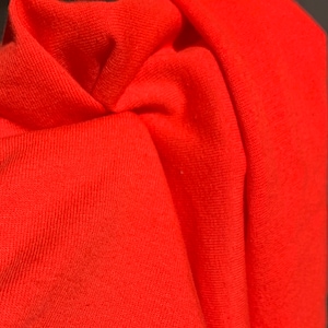 May include: Close-up of a bright orange fabric with a textured surface. The fabric is folded and shows the texture of the material.